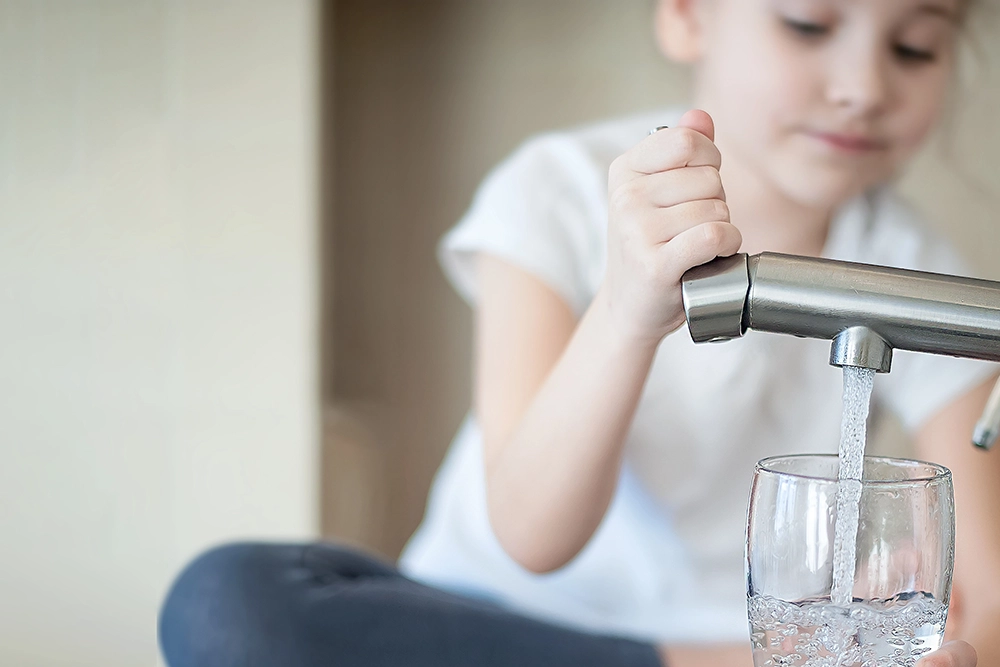 Mädchen zapft Wasser aus dem Wasserhahn in ein Glas.